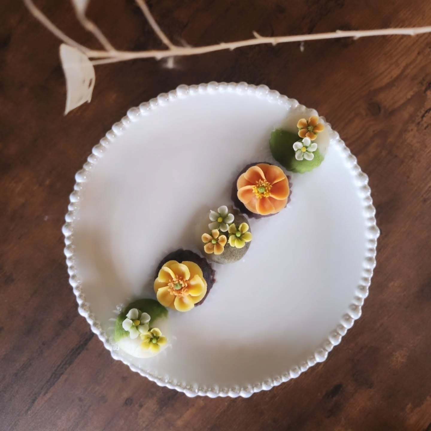 白い長皿に一列に並べた、花飾りのある緑茶やあんこのおはぎ